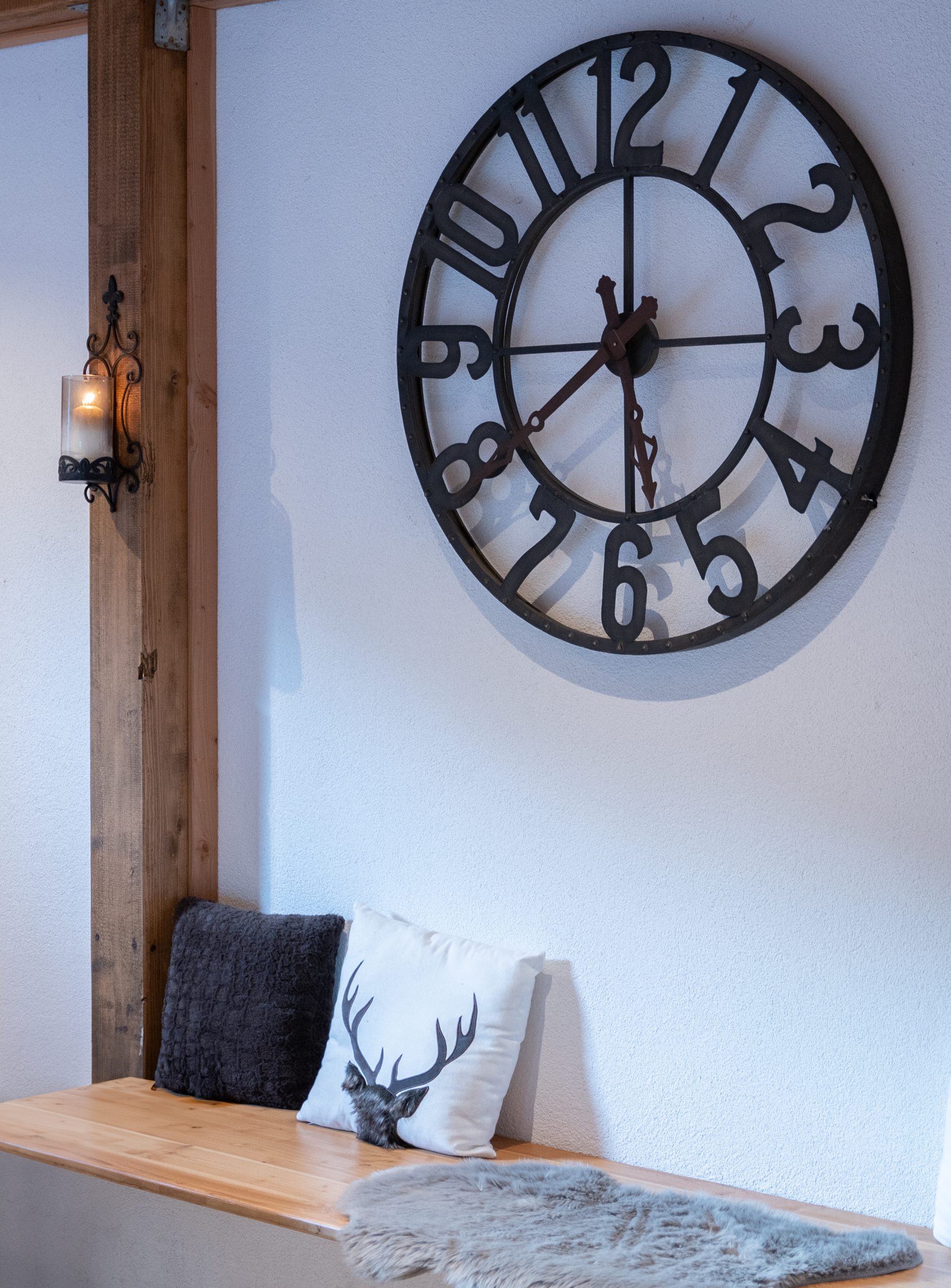 Große dekorative Wanduhr im Vintage-Stil an einer weißen Wand mit Holzbank und Kissen