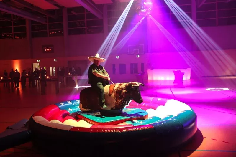 Mann mit Sombrero reitet auf mechanischem Stier bei einem Firmenevent mit pinker Beleuchtung