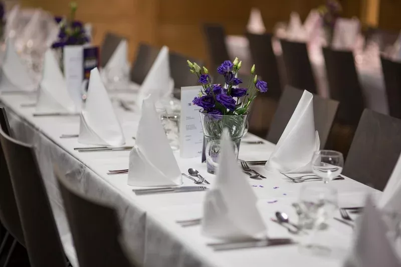Gedeckter Tisch mit Stoffservietten und lila Blumen bei Firmenevent
